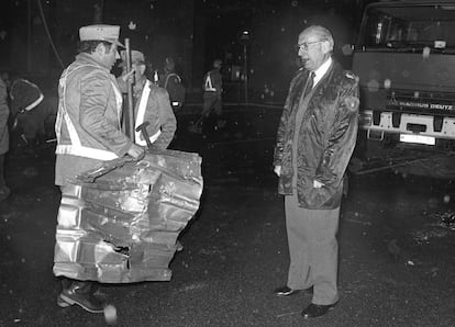 El alcalde de Madrid, Enrique Tierno Galván, vestido con un chubasquero de suboficial de la Policía Municipal, habla con dos barrenderos tras el atentado de ETA contra la sede de Telefónica en la calle de Ríos Rosas de Madrid, en abril de 1982.