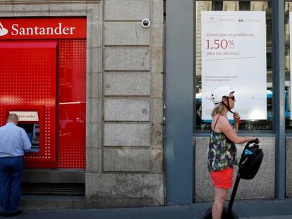 Un hombre sacando dinero de un cajero de Banco Santander, mientras otro pasa por delante de una oficina de Banco Popular