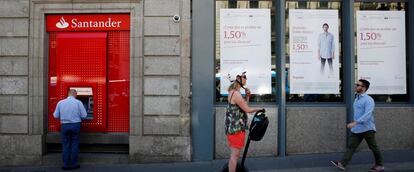 Un hombre sacando dinero de un cajero de Banco Santander, mientras otro pasa por delante de una oficina de Banco Popular