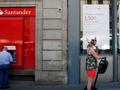 Un hombre sacando dinero de un cajero de Banco Santander, mientras otro pasa por delante de una oficina de Banco Popular