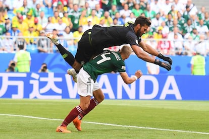 O goleiro brasileiro Alisson pula sobre Javier Hernández durante uma jogada.