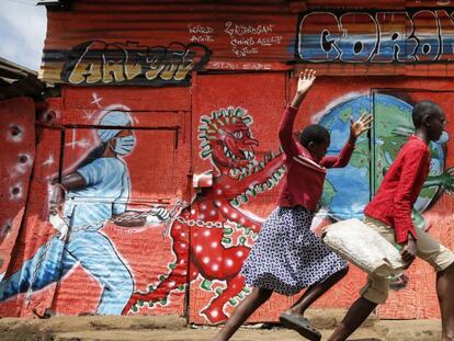 Dos niños corren por una calle frente a un mural informativo que advierte del peligro de la covid-19, en el barrio marginal de Kibera (Kenia).