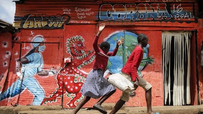 Dos niños corren por una calle frente a un mural informativo que advierte del peligro de la covid-19, en el barrio marginal de Kibera (Kenia).