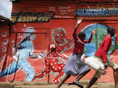 Dos niños corren por una calle frente a un mural informativo que advierte del peligro de la covid-19, en el barrio marginal de Kibera (Kenia).