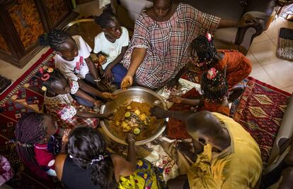 Thioro Amar (abajo, con falda amarilla) y su familia almuerzan un plato de 'thiebudienne' en su vivienda del barrio de Pikine, en Saint Louis, Senegal.