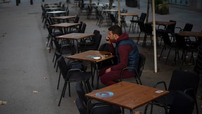 A customer sits at an empty sidewalk café in Barcelona, where new restrictions on the food service industry will come into effect on Monday.