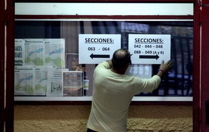 Un hombre coloca carteles informativos en un colegio electoral de Madrid durante la jornada de reflexión.