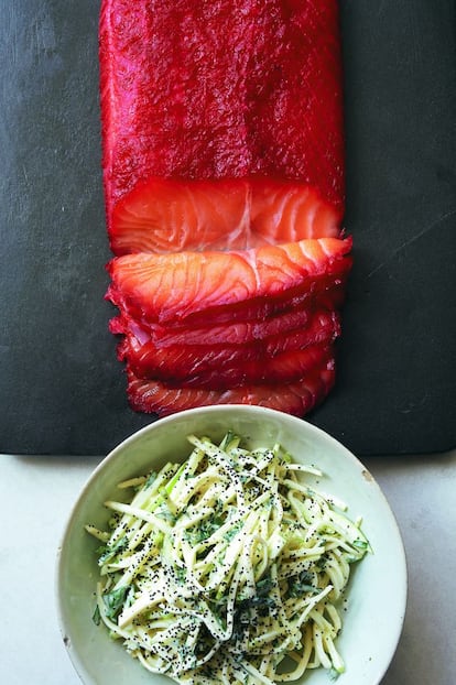 <p><b>La capa exterior </b>del salmón toma el color rojo de la remolacha y crea un efecto impresionante. A la ensalada de manzana y apionabo (inspirada en la francesa con mahonesa y mostaza) se añade manzana para contrarrestar la acidez del limón.</p><p><i> Ingredientes</i></p><p> Marinada: 2 cucharadas de semillas de cilantro, 250 gramos de remolacha cruda, pelada y rallada, la ralladura de 2 naranjas, 100 gramos de sal marina fina, 100 gramos de azúcar extrafino, pimienta negra recién molida. Ensalada: el zumo de 1 limón, 1 apionabo grande pelado, 2 manzanas granny smith partidas en cuartos y descorazonadas, 300 mililitros de nata agria, 2 cucharadas de mayonesa de buena calidad, 2 cucharadas de hojas de perejil finamente picadas, 2 cucharadas de semillas de amapola, sal y pimienta. Además, 800 gramos de lomo de salmón sin escamas ni aletas, pero con la piel, y pan de centeno. </p><p><i> Preparación</i></p><p> 1. Forrar con film transparente una bandeja suficientemente grande para que quepa el salmón y colocarlo con la piel hacia abajo. 2. Triturar las semillas de cilantro en un mortero. Colocarlas en un bol con la remolacha, la ralladura de naranja, la sal marina, el azúcar y un poco de pimienta negra, y mezclar bien. 3. Extender la marinada sobre el salmón para recubrirlo completamente. Taparlo con film transparente y colocar sobre él otra bandeja o fuente. Ponerle peso encima con algunas latas o una olla pesada y dejarlo marinar en la nevera unas 8 horas o toda la noche. Antes de servirlo, preparar la ensalada: cortar el apionabo y las manzanas en juliana y mezclarlo enseguida con el zumo de limón para evitar que se oscurezca. En un recipiente aparte, mezclar la nata agria, la mayonesa y el perejil. Salpimentar, añadir la salsa a la ensalada y remover bien. Probar y rectificar la sazón si es necesario. Sacar el salmón de la marinada y escurrirlo. Colocar el pescado en una tabla con la piel hacia abajo y cortar diagonalmente lonchas finas de 1 o 2 milímetros de grosor, girando el cuchillo al llegar a la piel para desprender la carne de ella. Poner los trozos de salmón en una fuente. Adornar la ensalada de manzana y apionabo con las semillas de amapola y servirla con el salmón y un poco de pan de centeno tostado.</p>