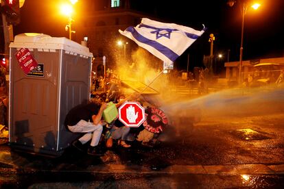 Maniefestantes israelíes se protegen del cañón de agua de la policía durante las protestas en la madrugada del 26 de julio de 2020 en las inmediaciones de la residencia de Benjamín Netanyahu en Jerusalén.