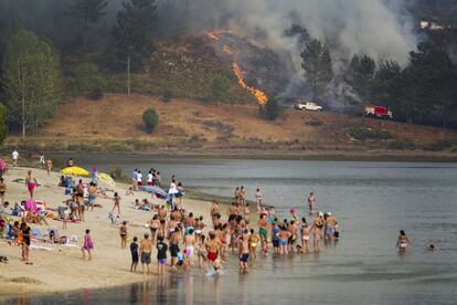 Los incendios forestales en Galicia engullen más de 1.500 hectáreas desde el lunes. En la imagen, bañistas en Ponte Sampaio contemplan desde la playa el fuego que arrasa el monte, el 10 de agosto.