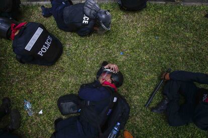 Policías antidisturbios se cubren el rostro con pañuelos mojados mientras los manifestantes anti gubernamentales les lanzan botes de gas lacrimógeno.