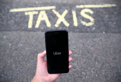 Una persona sostiene un móvil con la aplicación de Uber frente a una parada de taxis.