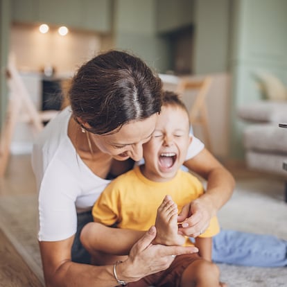 Mother tickling her little son's foot in living room at home.