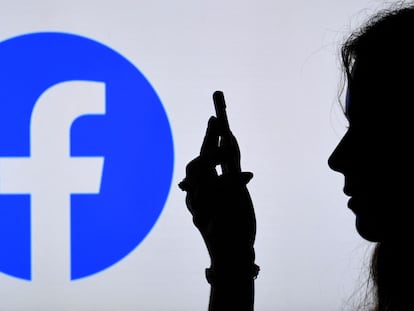 Una persona mira un 'smartphone' con el logotipo de la aplicación de Facebook de fondo.