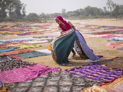 Un niño recoge unos tejidos después de secarse al sol en India.