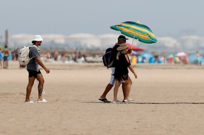 Dos personas se protegen del sol bajo una sombrilla en la playa de la Malvarrosa, en Valencia.