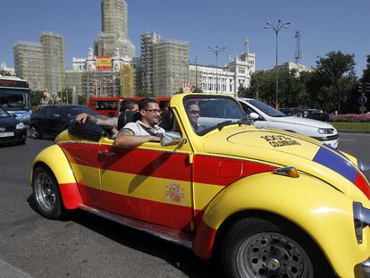 Un coche con la bandera de España circula por Cibeles ante el edificio del Ayuntamiento de Madrid.