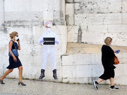 Mujeres con mascarilla pasean por Lisboa ante un cartel que dice "quédense en casa"