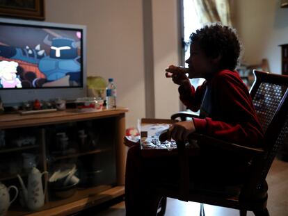 Un niño come un trozo de pizza del menú infantil de Telepizza mientras ve la televisión en su casa, en Usera.
