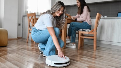 Una chica encendiendo el robot aspirador en la cocina de su casa.