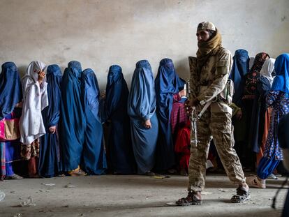 A Taliban fighter stands guard as women wait to receive food rations distributed by a humanitarian aid group, in Kabul, Afghanistan, on May 23, 2023.