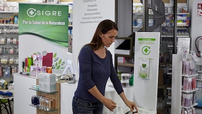Una mujer deposita medicamentos en desuso en el punto Sigre de una farmacia.