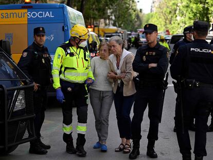 A first reponder assists two residents, as emergency services are searching for two people missing after a strong explosion injured 17 people in the Salamanca neighbourhood in Madrid, on May 6, 2022. - According to the latest report released by the emergency services, 17 injured have been taken care of. Four of them have been transferred to hospitals, including one in serious condition. (Photo by Pierre-Philippe MARCOU / AFP)