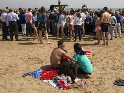 Una familia disfruta de la playa ante el paso de la procesion de la Semana Santa Marinera.