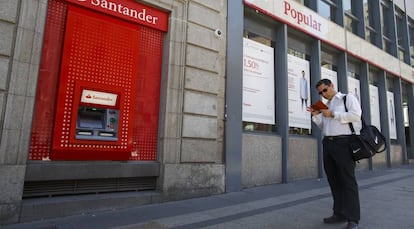 Un hombre pasea junto a una sucursal del Popular y un cajero del Santander.