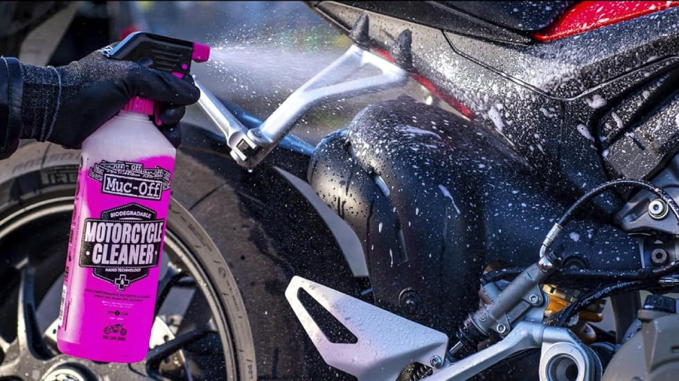 Una persona usa el limpiador especial Muc-off sobre la superficie de su moto.