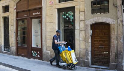 Un cartero pasa por delante de un bajo comercial en una calle de Barcelona.