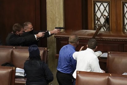 La policía del Capitolio de los Estados Unidos con armas en la mano observa cómo los manifestantes intentan irrumpir en la sala principal del Capitolio.