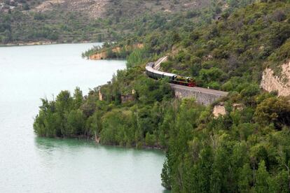 El tren atraviesa el pantano de Cellers, con apariencia de lago natural, en cuyo espejo de aguas tranquilas se reflejan los exuberantes bosques de ribera y las cumbres pirenaicas.