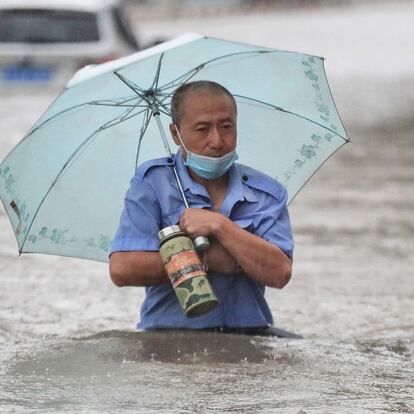This photo taken on July 20, 2021 shows a man wading through flood waters along a street following heavy rains in Zhengzhou in China's central Henan province. (Photo by STR / AFP) / China OUT