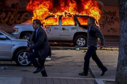 Miembros de la CICPC caminan frente a un vehículo incendiado durante una marcha convocada por la oposición, en Caracas (Venezuela).