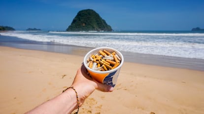 Un vaso de plástico reutilizado como cenicero en la playa.