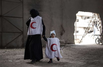 Una mujer y su hijo esperan, con el peto de la Media Luna Roja, a ser trasladados desde un control rebelde del barrio de Bustan al-Qasr, en Alepo, hasta una zona controlada por el régimen.