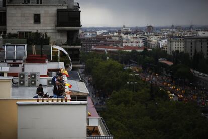 Un grupo de personas con banderas nacionales miran desde la azotea de un edificio el desfile militar de las Fuerzas Armadas en Madrid.
