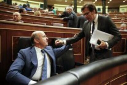 El ministro de Economía, Luis de Guindos, conversa con el diputado socialista Javier Moscoso, al inicio de la sesión de control al Ejecutivo que se celebra en el Congreso de los Diputados.