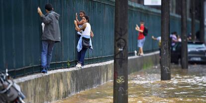 Varias personas se apoyan en una cerca para atravesar una calle inundada.