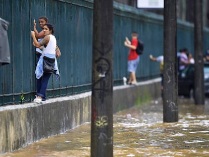 Varias personas se apoyan en una cerca para atravesar una calle inundada.