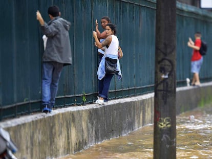 Varias personas se apoyan en una cerca para atravesar una calle inundada.