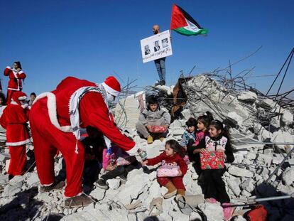 Un manifestate palestino vestido de Papá Noel entrega regalos a unos niños en los restos de una casa demolida por Israel en Belén.