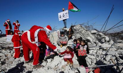 Un manifestate palestino vestido de Papá Noel entrega regalos a unos niños en los restos de una casa demolida por Israel en Belén.