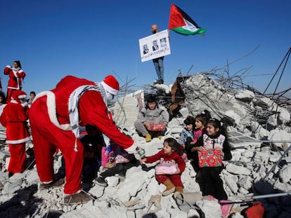 Un manifestate palestino vestido de Papá Noel entrega regalos a unos niños en los restos de una casa demolida por Israel en Belén.