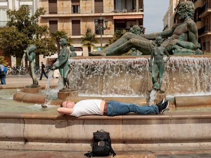 Un hombre descansa al sol en la fuente de la plaza de la Virgen de Valencia, el pasado viernes.