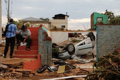 Escombros y un auto volcado junto a residentes luego de que un ciclón extratropical azotara ciudades del sur, en Roca Sales.