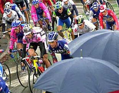 El público se protege de la lluvia al paso del pelotón.