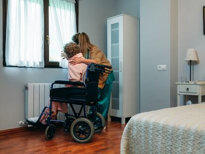 Una cuidadora muestra la vista por la ventana a una mujer en silla de ruedas.