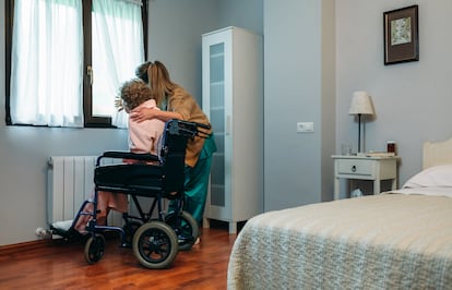 Una cuidadora muestra la vista por la ventana a una mujer en silla de ruedas.